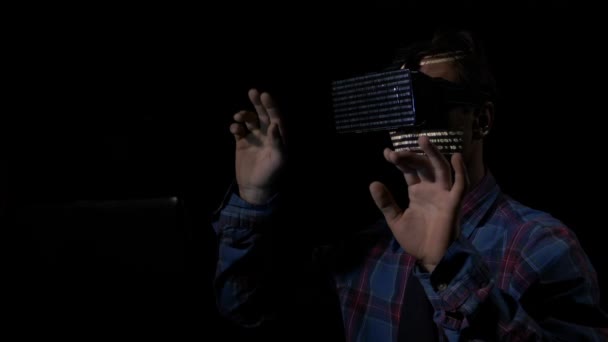 Mannelijke hacker gebruikt een vr headset voor zijn programmering, terwijl witte code tekens op zijn gezicht weerspiegelen — Stockvideo