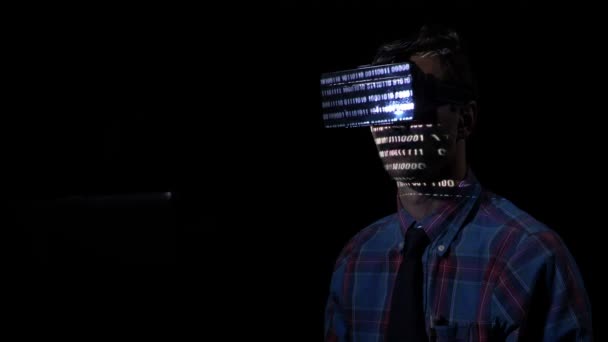 Software developer experiencing virtual reality goggle glasses at night in a dark room to read binary codes reflected on his face — Stock Video