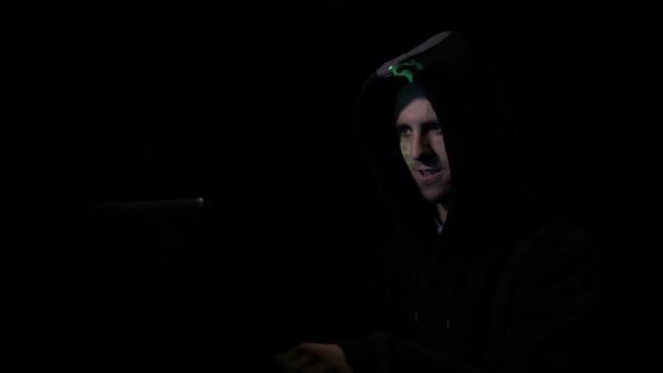 Cyber criminel dans la capuche assis dans le commerce sombre sur les serveurs de devises Bitcoin et parler au téléphone tandis que le symbole se reflète sur son visage 