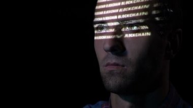 Blockchain sembolü yüzünde yansıtılır iken bir monitör ekranına bakarak sakallı yetişkin bir adam yakın çekim