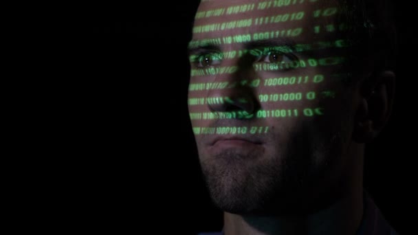 Gros plan d'un hacker adulte barbu travaillant sur un ordinateur tandis que des caractères de code vert sont projetés sur son visage — Video