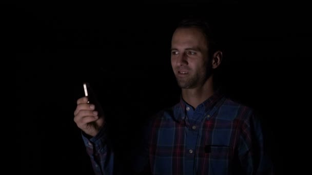 Бізнесмен сидить у темній кімнаті і сканує своє обличчя за допомогою смартфона з додатком розпізнавання обличчя, щоб розблокувати його — стокове відео