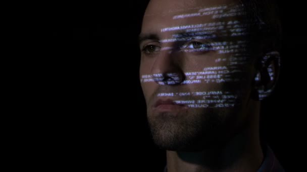 Крупный план взрослого программиста-мужчины, работающего в темной офисной комнате, пока последовательный код отражается на его лице — стоковое видео
