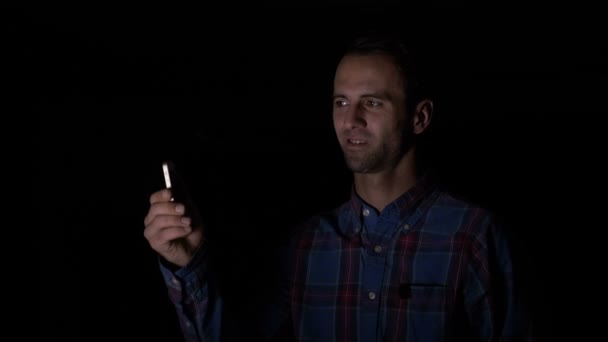 Empresario sentado en una habitación oscura y escaneando su rostro con un smartphone con aplicación de reconocimiento facial para desbloquearlo — Vídeo de stock