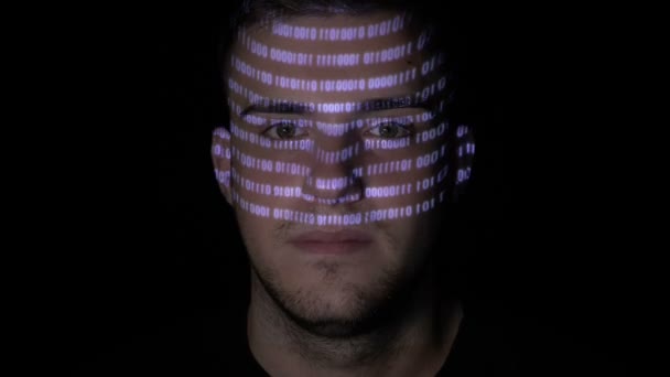 Running digital binary data code reflected on the face of a young man working on computer in the dark — Stock Video