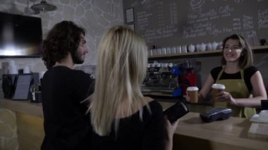 Yavaş hareket dostu olurken kahve için ödemek için smartphone kullanarak bir kafe dükkanda genç bir çiftin bir kadın Kahveci tarafından hizmet