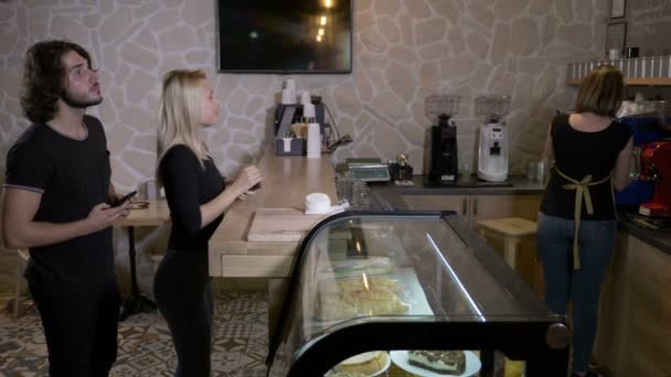 年轻和美丽的客户在咖啡店订购饮料和支付 cryptocurrency 比特币使用他们的智能手机 — 图库视频影像