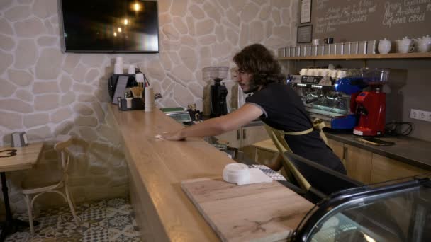 Barista homem limpando o balcão quando um cliente feminino vem em flertes com ele ordens de um café para ir e paga com moeda criptomoeda bitcoin — Vídeo de Stock