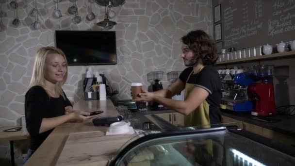 Maschio barista serve e flirta con una bella cliente donna che paga utilizzando l'app smartphone in una caffetteria al rallentatore — Video Stock