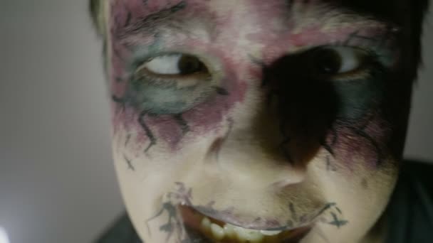 Närbild på en ung pojke som bär halloween zombie ansikte färg smink och kostym ser direkt till kameran — Stockvideo
