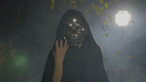 Assustador zumbi escuro usando uma máscara brincando com sua capa preta atacando a câmera no dia das bruxas luar — Vídeo de Stock