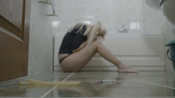 Депресивна приваблива жінка сидить на підлозі у ванній і думає про свої проблеми з жалем після того, як героїн застрелився в її венах — стокове відео