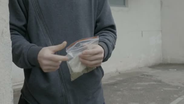 Homme dealer assis au coin de la rue essayant de convaincre un client d'acheter un petit sac de marijuana à un bon prix — Video