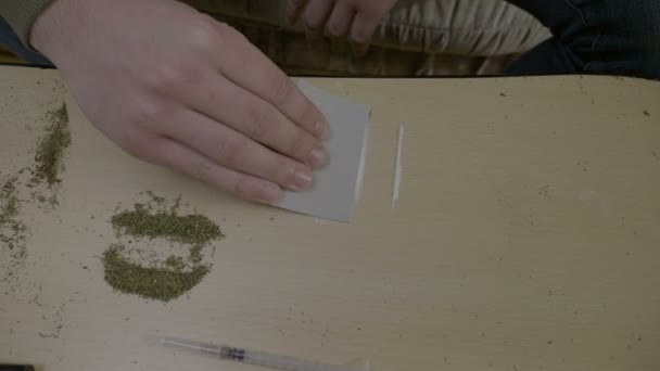 Close up of an addicted male hacker sitting on the couch separating cocaine into thin lines to be snorted directly from the table — Stock Video