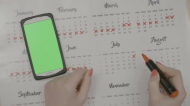 Kadının üstten görünüm takvim günü doğum önleme ile yeşil ekran smartphone izleme dönem planlama üzerinde geçerken eller