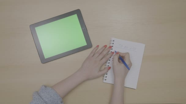 Bovenaanzicht van vrouw handen planning om lijst te doen bij groen scherm tablet-pc en schrijven op Kladblok — Stockvideo