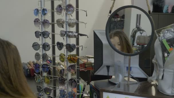 Ganska ung tonåring flicka försöker olika märken av solglasögon i en butik — Stockvideo