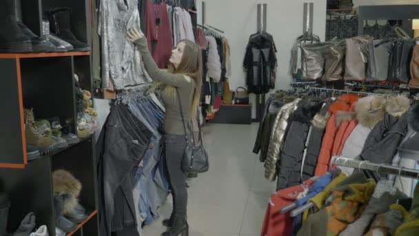 Atractiva modelo femenina con tacones que navega por ropa para comprar en un centro comercial — Vídeo de stock