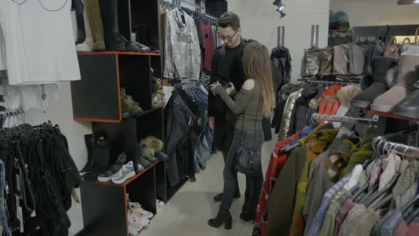 年轻的学生夫妇走在服装店商场寻找合适的鞋子和衬衫买的女朋友 — 图库视频影像