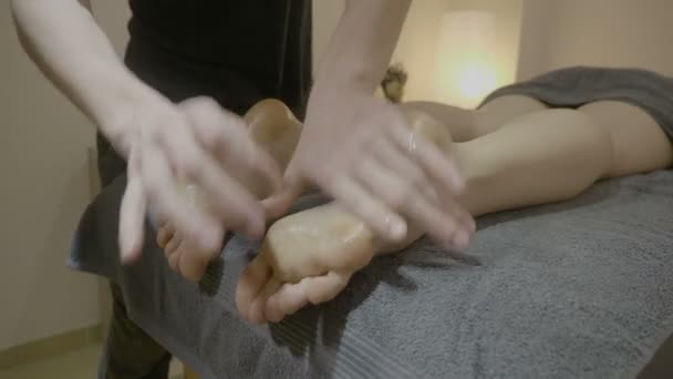 Профессиональный молодой массажист массирует ноги клиента маслом и нежно массирует их в спа-центре — стоковое видео