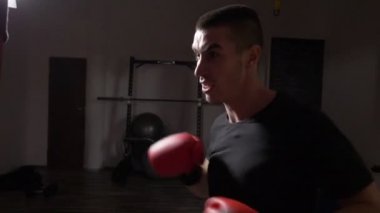 Kırmızı boks eldiven giymiş ve kum torbası ağır çekimde endişeyle isabet genç atletik boksör profili