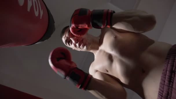 Low shot of fit hemdloser Boxer, der hart mit dem Boxsack in Zeitlupe trainiert — Stockvideo