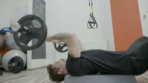 Primer plano de un atractivo hombre hermoso levantando pesas en un gimnasio mientras está acostado en una prensa de banca — Vídeo de stock