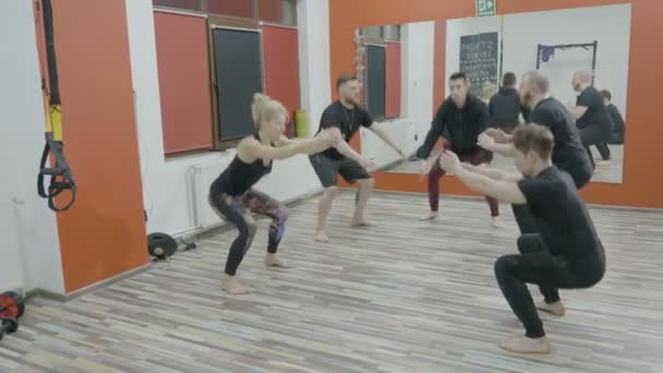 Vier aktive Jungen und ein Mädchen trainieren ihren Körper in einer Crossfit-Turnstunde, indem sie Kniebeugen machen — Stockvideo