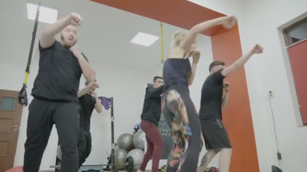 Energetico team di kickboxing motivato composto da uomini e una ragazza bionda che si riscalda in una palestra in studio con esercizi di colpire — Video Stock