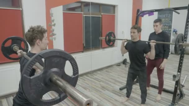 Αρσενικό βάρη και κάνουν καταλήψεις για να λειτουργήσει το σώμα του μύες στο γυμναστήριο με τη βοήθεια ενός προσωπικού γυμναστή — Αρχείο Βίντεο
