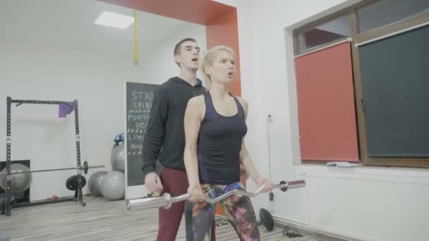 Γυναίκα bodybuilder σε αθλητικά ενδύματα εργασίας με βαρέα βάρη στο γυμναστήριο, ενώ το προσωπικό γυμναστή διορθώνει τη στάση του σώματος και ασκήσεις — Αρχείο Βίντεο