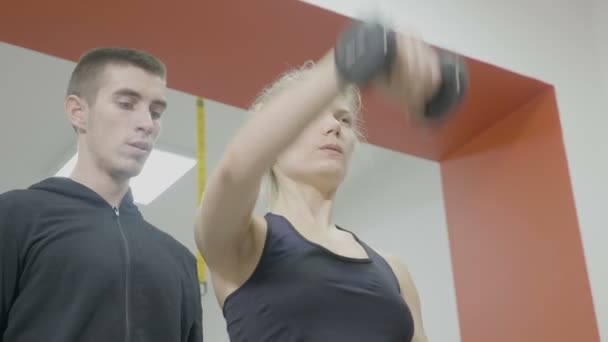 Mooie fit vrouw haar armen met halters in de sportschool trainen met haar vriendje personal trainer — Stockvideo