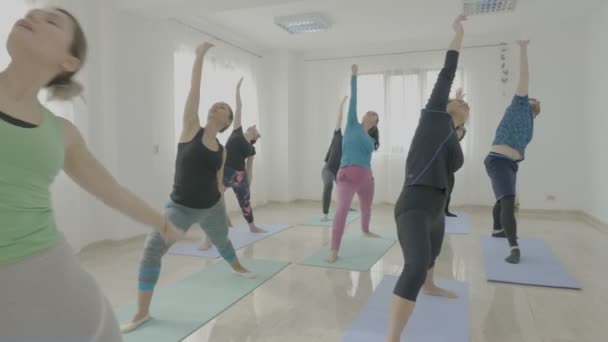 Yoga-Kurs mit Frauen mittleren Alters und einem jungen Mann, der neue Posen ausprobiert und auf seine Dozentin hört — Stockvideo