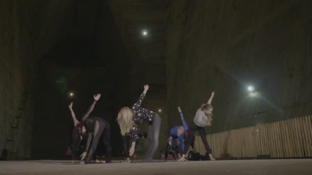 Skinny fit femmes échauffement avec des exercices d'étirement pour la séance de yoga tenue par un maître instructeur dans une mine souterraine profonde sombre de sel froid — Video