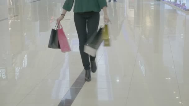 Primer plano de la divertida mujer feliz en tacones llevando bolsas de compras caminando de una manera de moda girando y bailando en el centro comercial — Vídeos de Stock