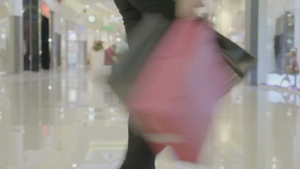 Close up van de benen van de vrouw in donkere broek lopen en spinnen bij het winkelcentrum bij de uitvoering van boodschappentassen in beide handen — Stockvideo