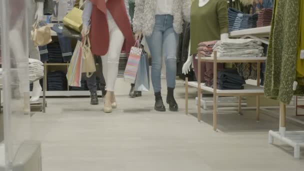 Молодые привлекательные покупательницы смотрят на одежду в торговом центре и медленно идут к камере — стоковое видео