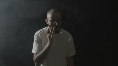 Duman teneffüs edilmesi ve çeşitli vaping pratik gözlüklü genç adam yapma çevrelerin karanlık bir odada hileci