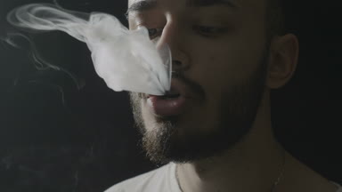 Bir Buharlaştırıcı teneffüs edilmesi ve vaping hile yaparken büyük miktarda duman exhaling sakallı genç hippi biri yakın çekim