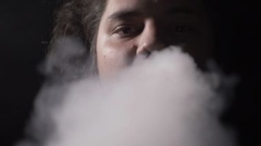Anti kampanya ile bir genç adam aktör uzun saç vaping elektronik sigara ile sigara ve ağır çekim kamera içine Buhar bulutu üfleme