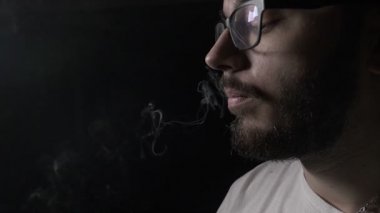 Genç genç öğrenci çocuk onun burun ve daha sonra ağzını ağır çekimde duman üfleme sakal bıyık ve gözlük vaping elektronik sigara ile