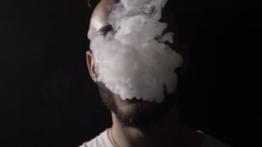 Cesur genç erkek müzisyen vaper sakal vapes ve onun büyük yavaş yüzünü örten vape duman bulutu dudağında darbeler ile