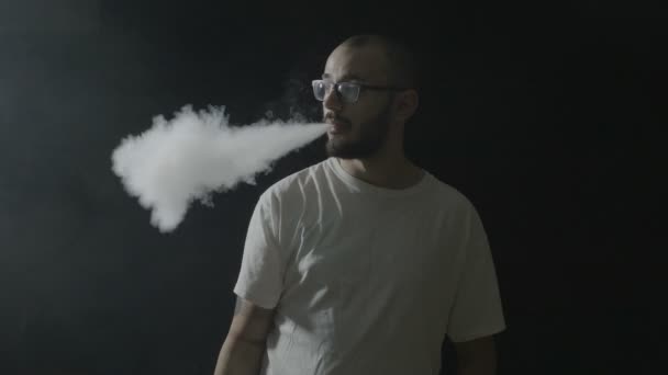 Ragazzo adolescente vaping divertirsi inalando da un vaporizzatore ed espirando il fumo verso la fotocamera su uno sfondo scuro — Video Stock