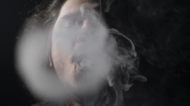 Slow motion porträtt av en skäggig tonåring pojke utför cirkel rök tricks efter vaping från en spridare i en professionell mörka studio — Stockvideo