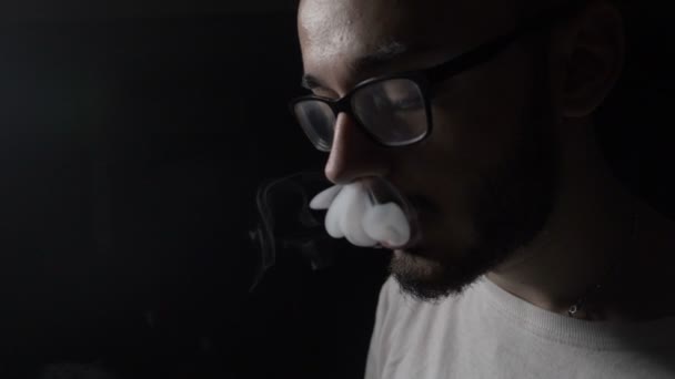 Sad depressed young IT engineer boy with glasses performing vaping tricks in a dark room in slow motion — Stock Video