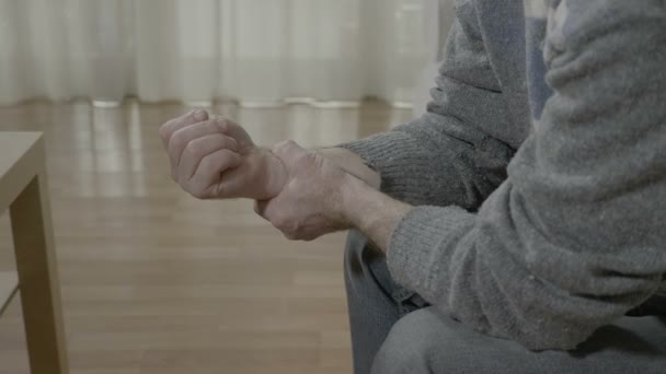 Nahaufnahme eines alten Mannes mit Arthritis, der sein schmerzhaftes Handgelenk berührt und Rheuma hat, der zu Hause auf der Couch sitzt — Stockvideo