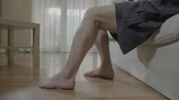 Closeup ξυπόλυτος ανώτερος άνθρωπος έχοντας δυσφορία των μυών του ποδιού, ενώ αυτός όρθιος από τον καναπέ — Αρχείο Βίντεο