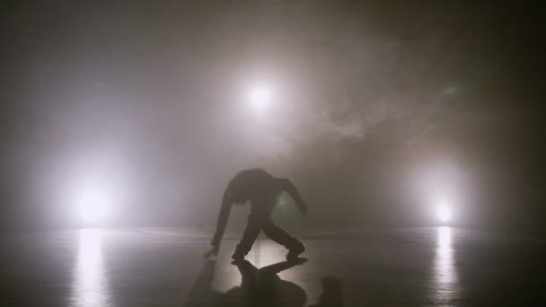 Bailarina masculina de hip hop con gorra realizando trucos de breakdance en el suelo con humo en el fondo — Vídeos de Stock