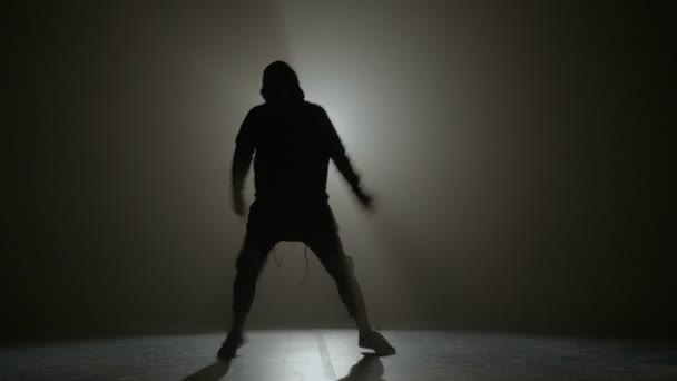 Silhouette of a young man in hood performing hip hop moves on a stage with spotlight in the background — Stock Video