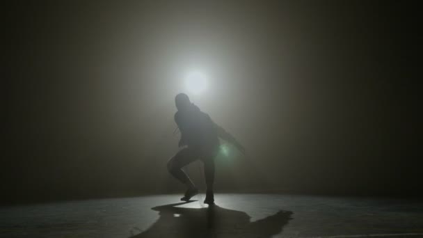 Silueta talentované mladé tanečnice tancující hip hop street dance na jevišti před reflektorem